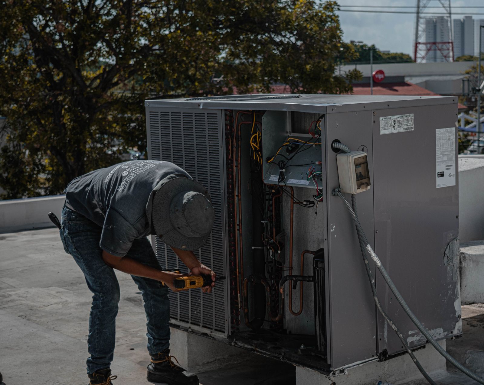 Technician repairing an outdoor air conditioner condenser unit on a rooftop